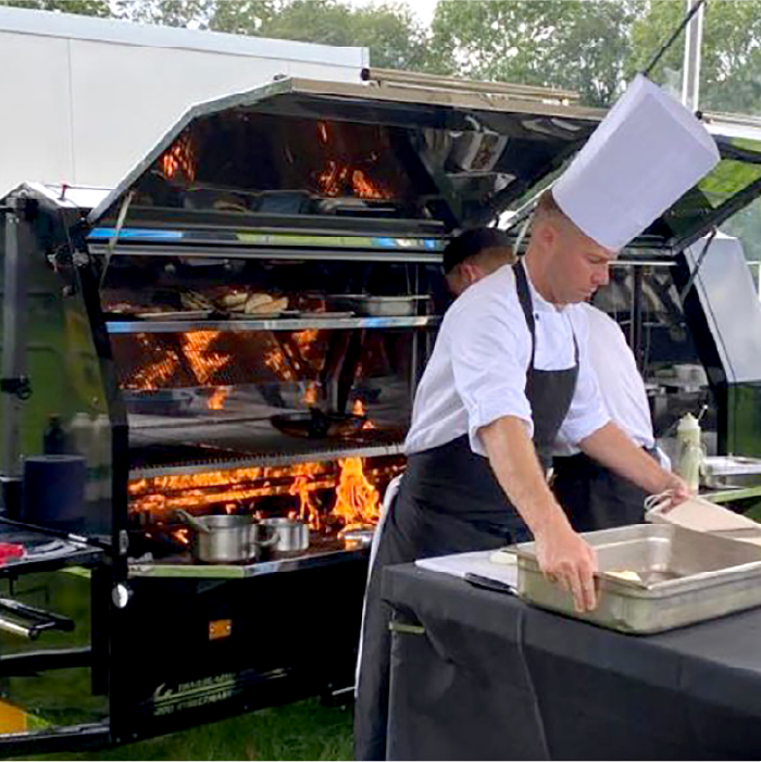 Chef preparing food in front of BBQ trailer for external event catering hire, Suffolk.